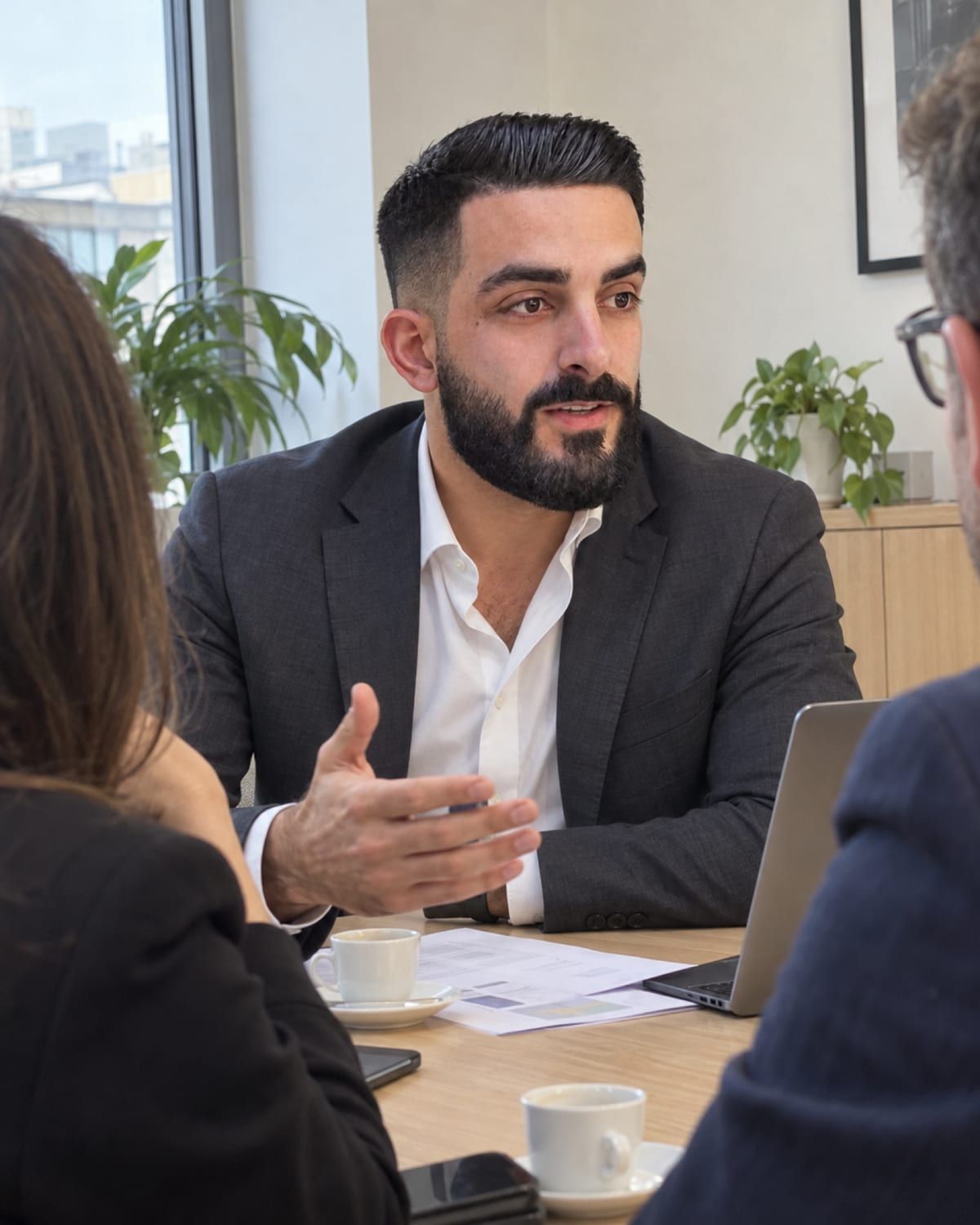 Francesco Sergio spiega un progetto a due clienti attorno a un tavolo con caffè e fogli